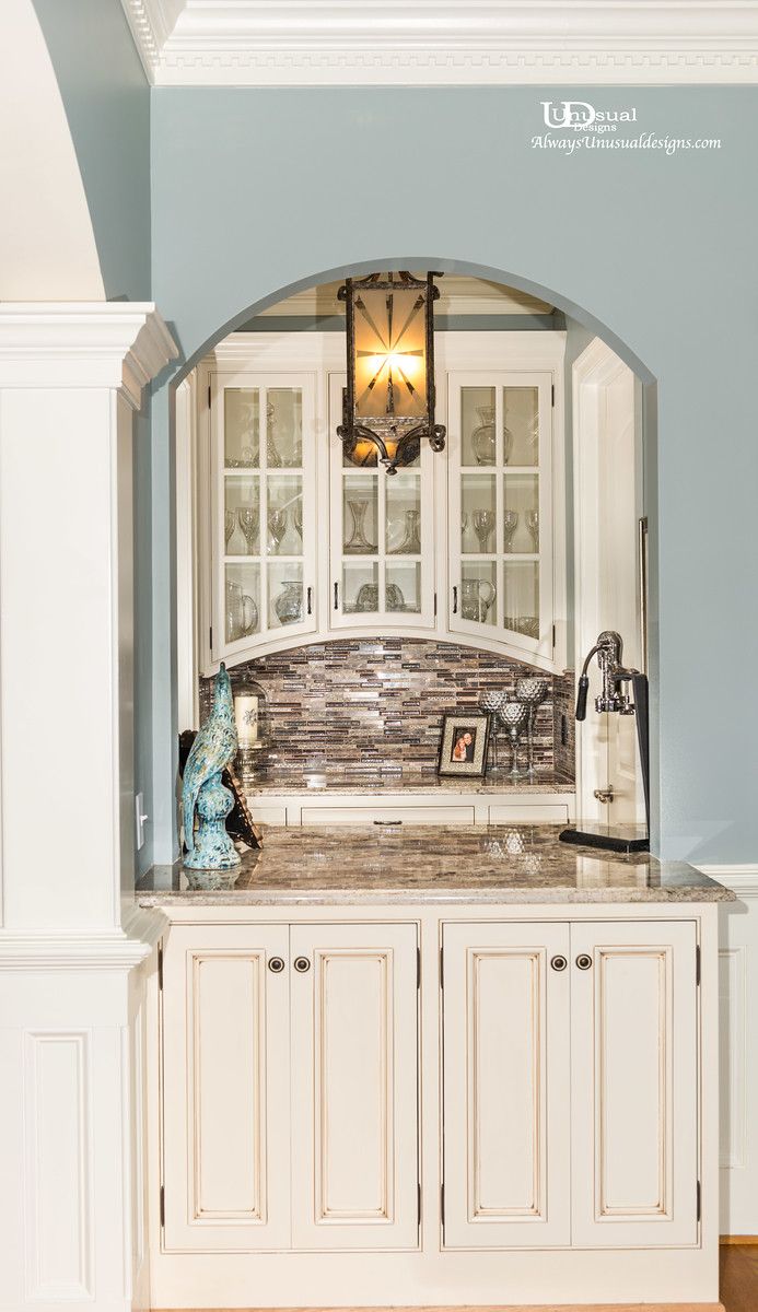 Built-in white cabinet with arched display, stone backsplash, and decorative lighting.