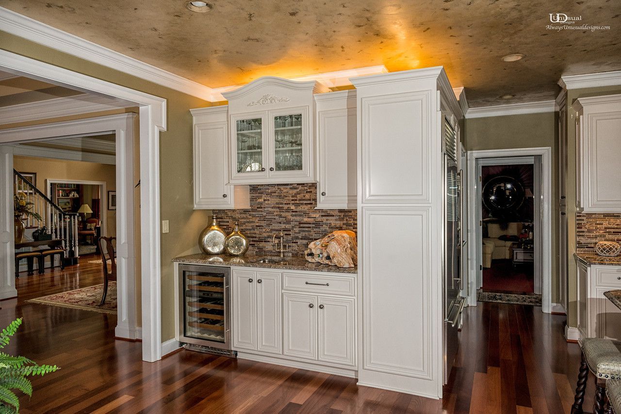 White built-in bar area with wine cooler, cabinets, and stone backsplash in a home.