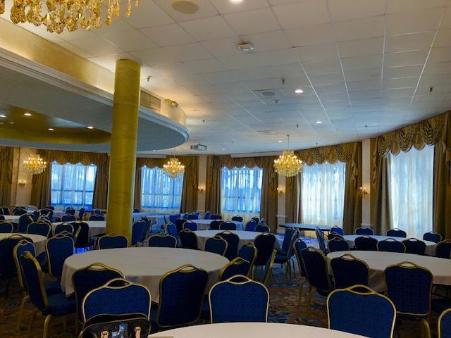 Banquet hall with round tables, blue chairs, gold accents, and chandeliers.