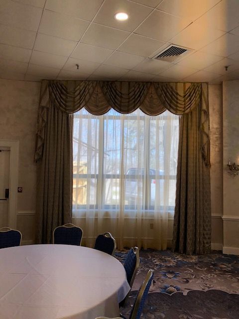 Large window with gold and beige curtains and valance in a room with a round table.