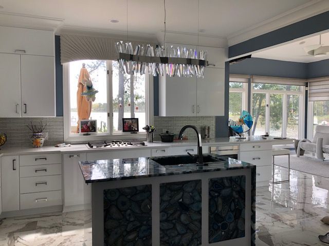 Modern kitchen with white cabinets, dark island, and a chandelier over a sink. Large windows with lake view.