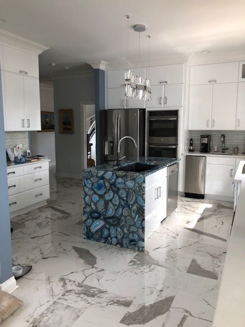 Spacious kitchen with a blue agate stone island, white cabinets, stainless steel appliances, and marble flooring.