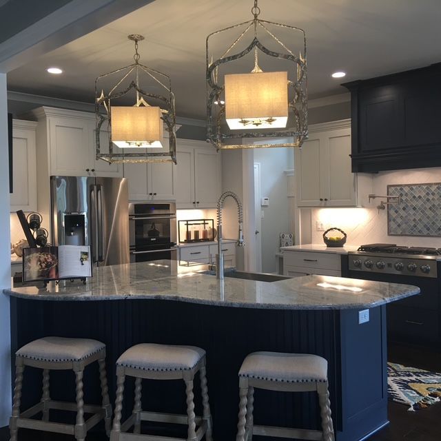 Kitchen with white cabinets, navy island, pendant lights, and three barstools.