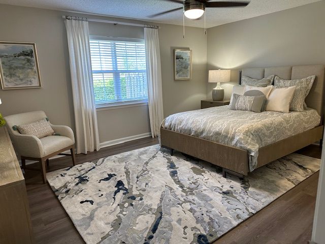 Bedroom with bed, chair, rug, window, and artwork. Neutral colors, modern design.