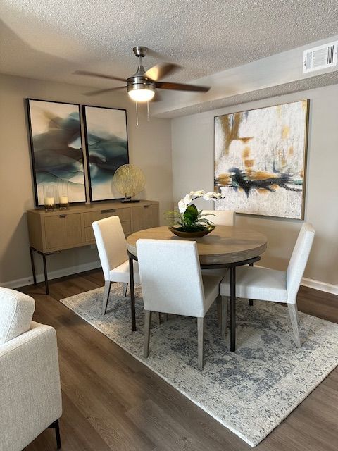 Dining room: Round table, four white chairs on a patterned rug, beige buffet, art, and ceiling fan.