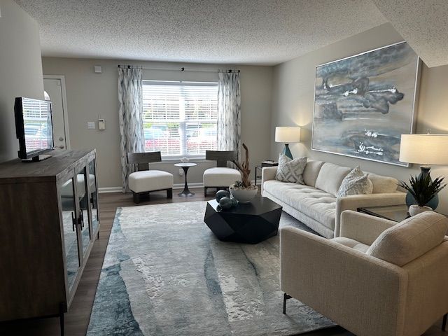 Living room with light-colored furniture, blue rug, large artwork, and a window with blinds.
