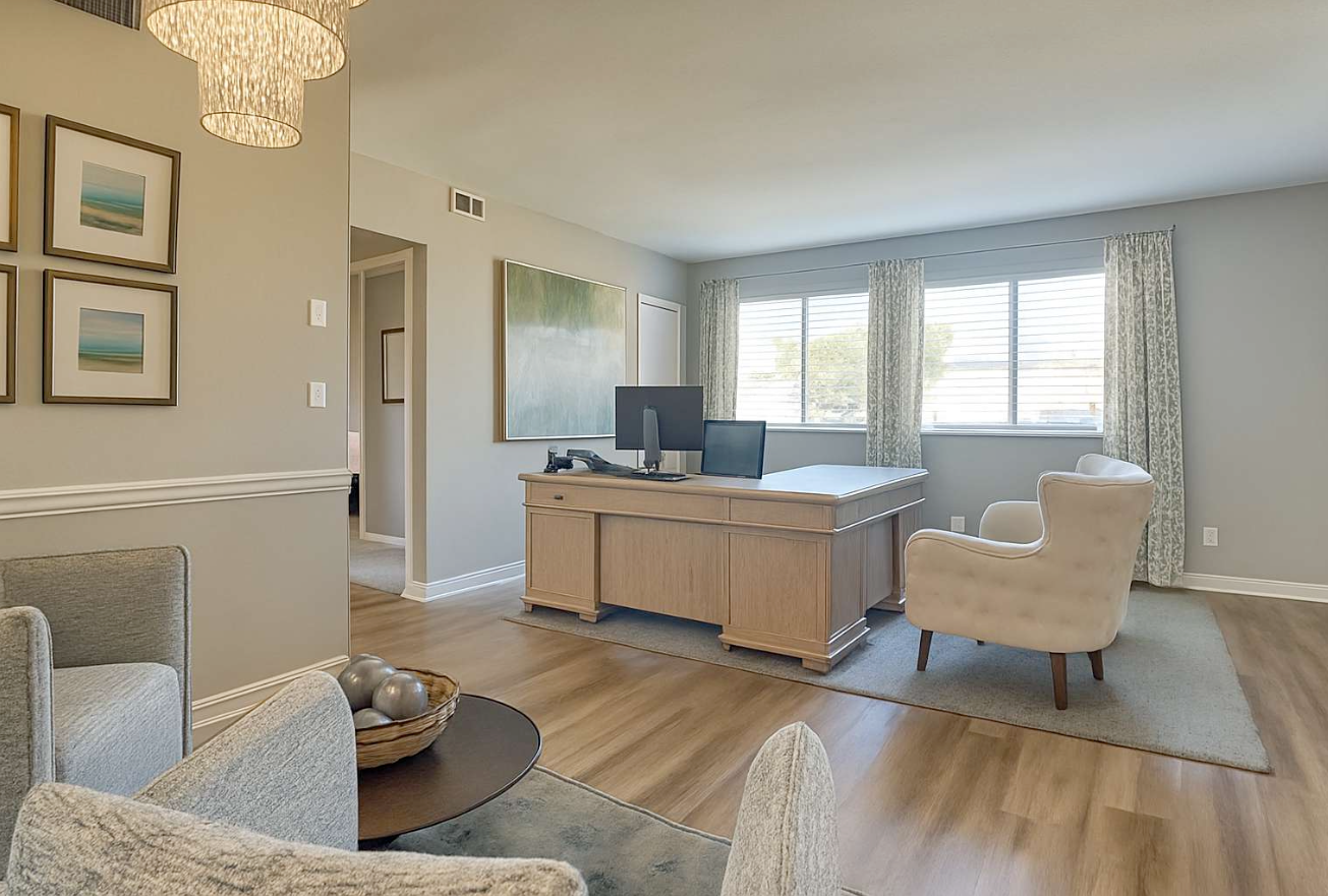 A home office with a desk, chairs, artwork, and natural light.