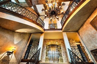 Ornate foyer with curved balconies, stone walls, and a large chandelier.