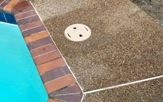 Pool coping with brick border, surrounded by textured concrete and a skimmer.