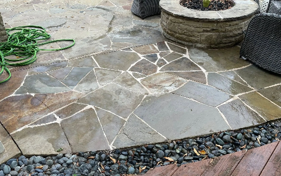 Flagstone patio with fire pit, surrounded by decorative rocks and a green hose.