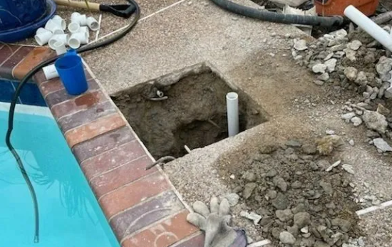 Pool repair: Square hole in patio, dirt, pipes, pool coping, blue water.