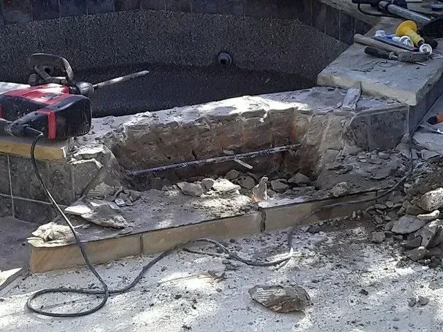 Construction site: broken pool steps with jackhammer, debris, and exposed rebar.