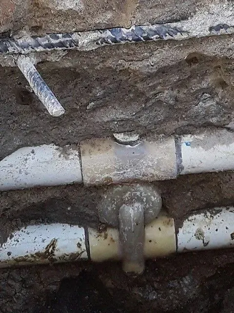 Pipes in a trench with a T-connector, a curved fitting, and a small piece of pipe above them.