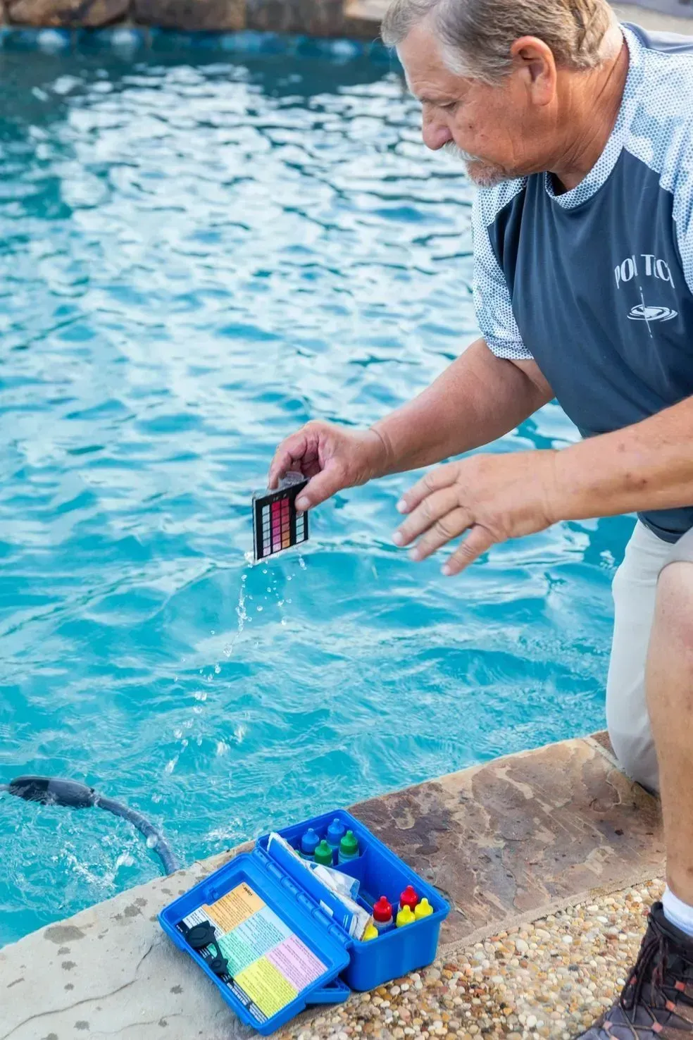 Man testing pool water with a test kit. Blue water, outdoor setting.
