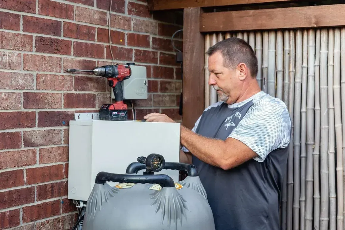 Man working on pool equipment next to a brick wall and bamboo screen.