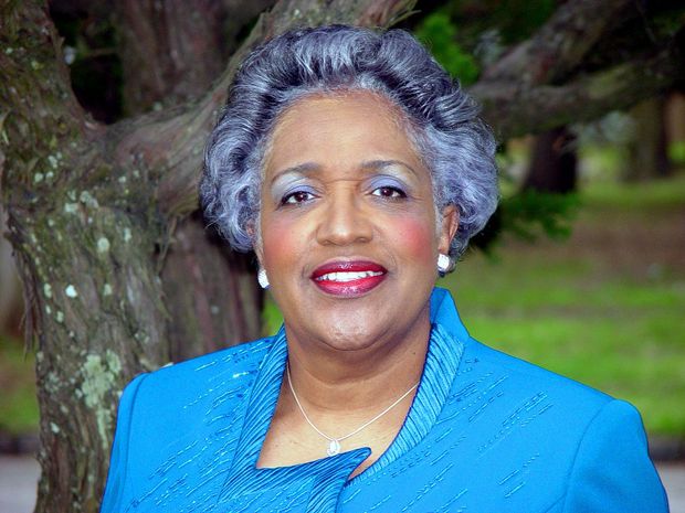 A woman in a blue jacket is smiling in front of a tree.