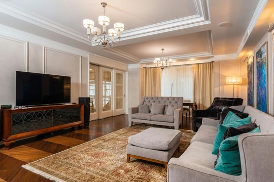 Living room with gray furniture, patterned rug, hardwood floors, and large-screen TV.