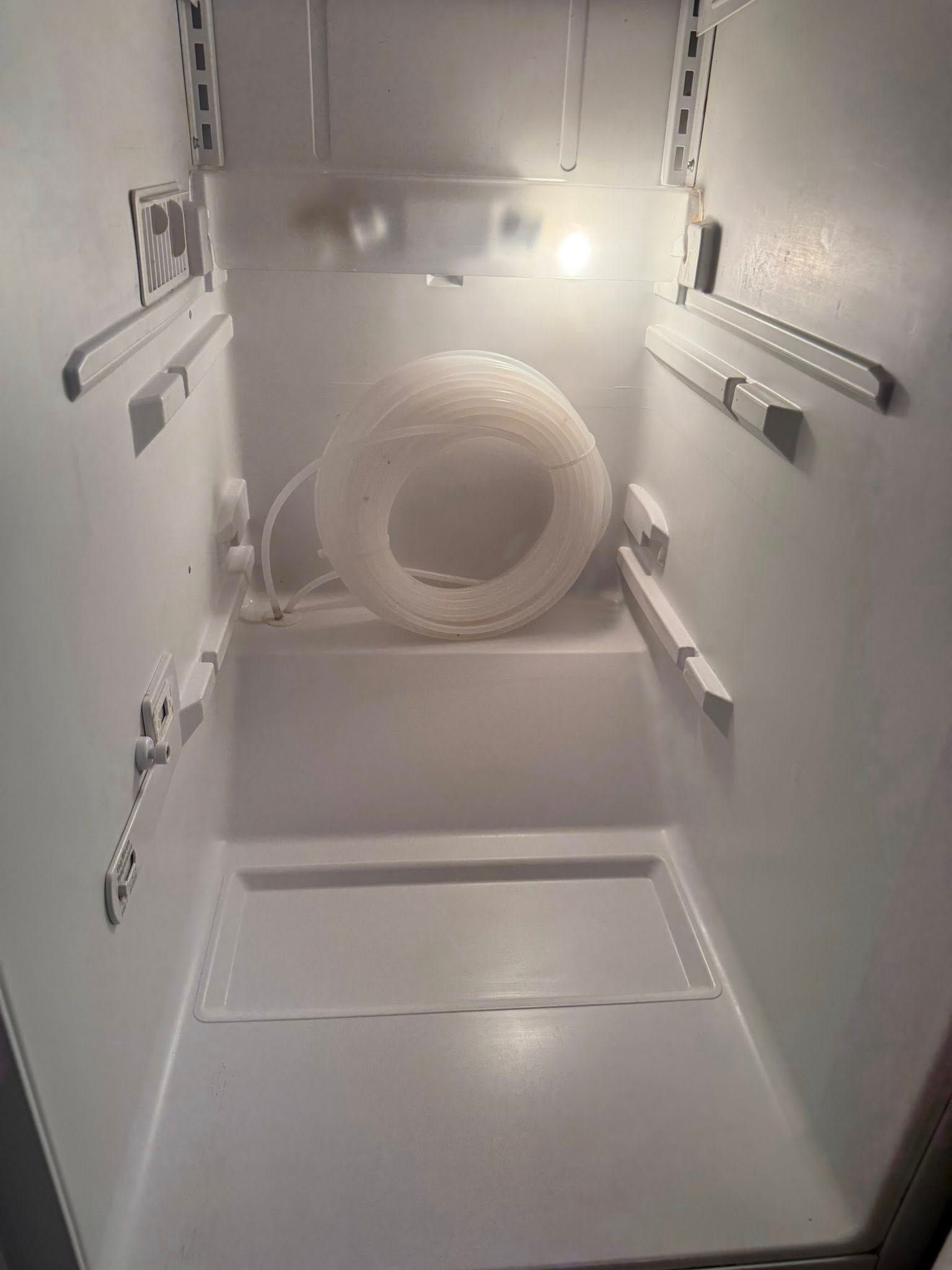 Empty white refrigerator interior with coiled white tubing.