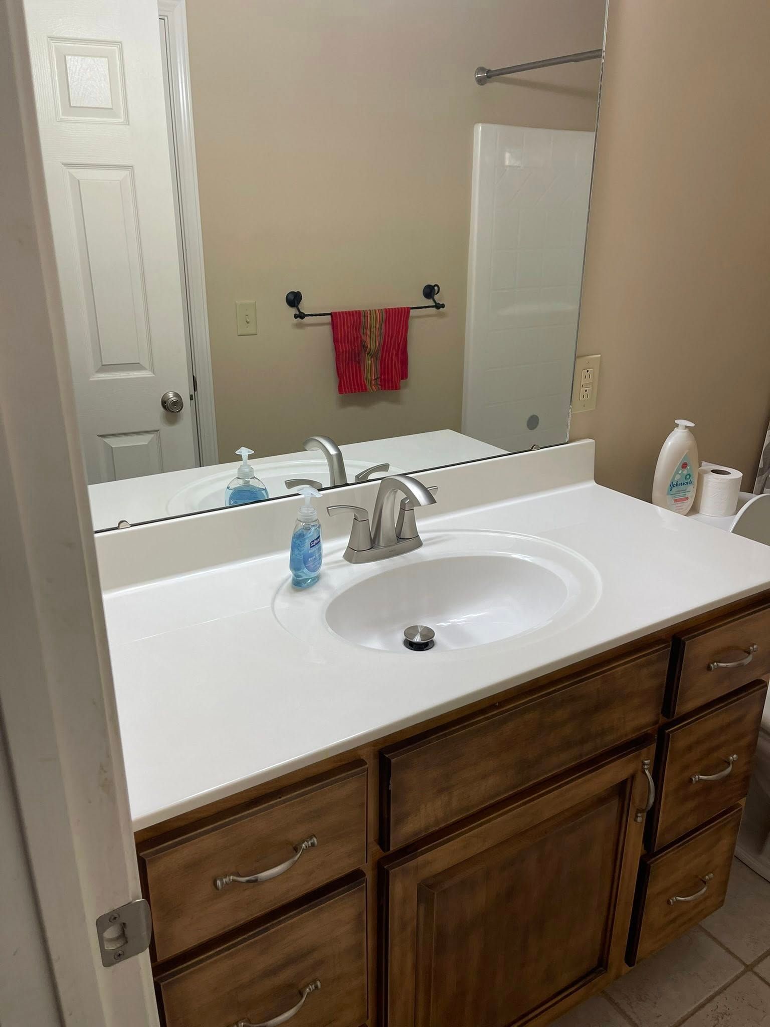 Bathroom with white countertop, oval sink, and wooden vanity with mirror reflecting a shower and door.