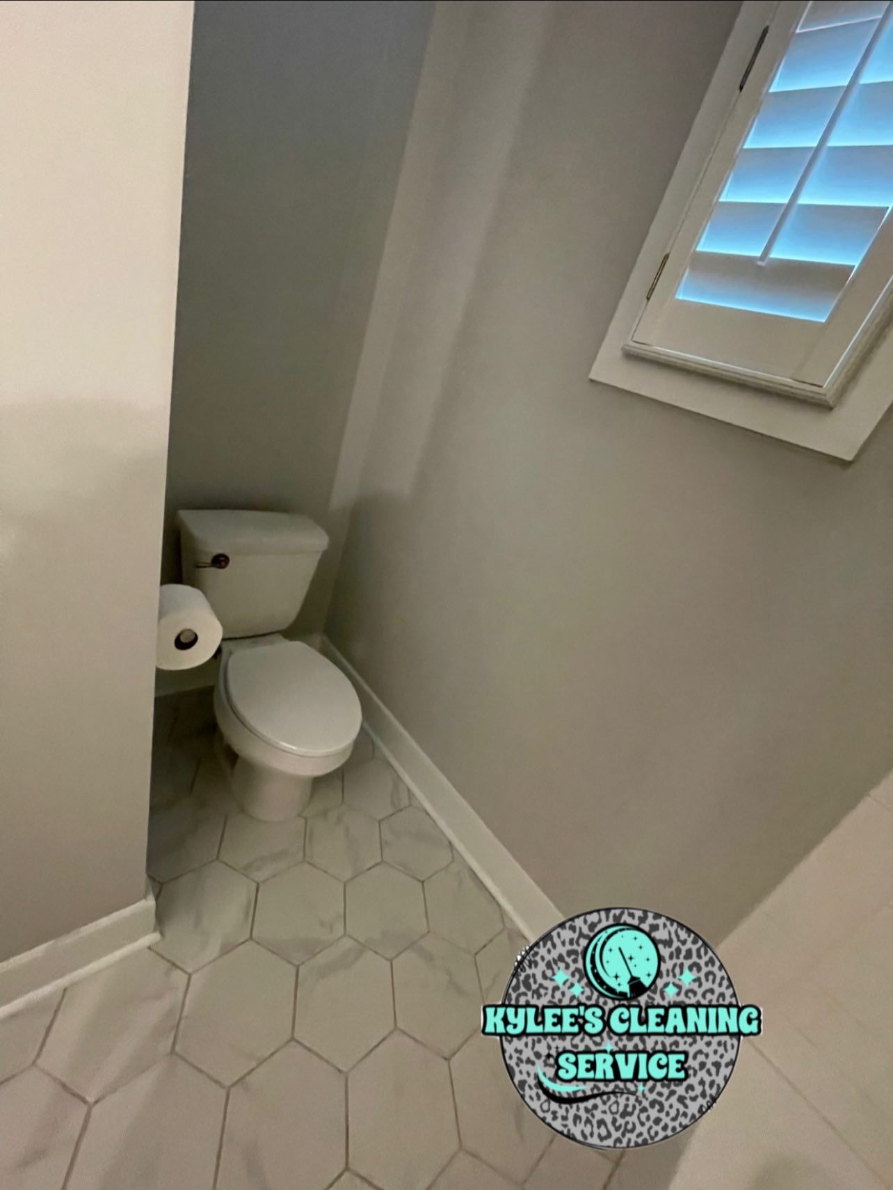 Toilet in a small, light-colored bathroom with hexagon-patterned floor tiles, and a window with shutters.
