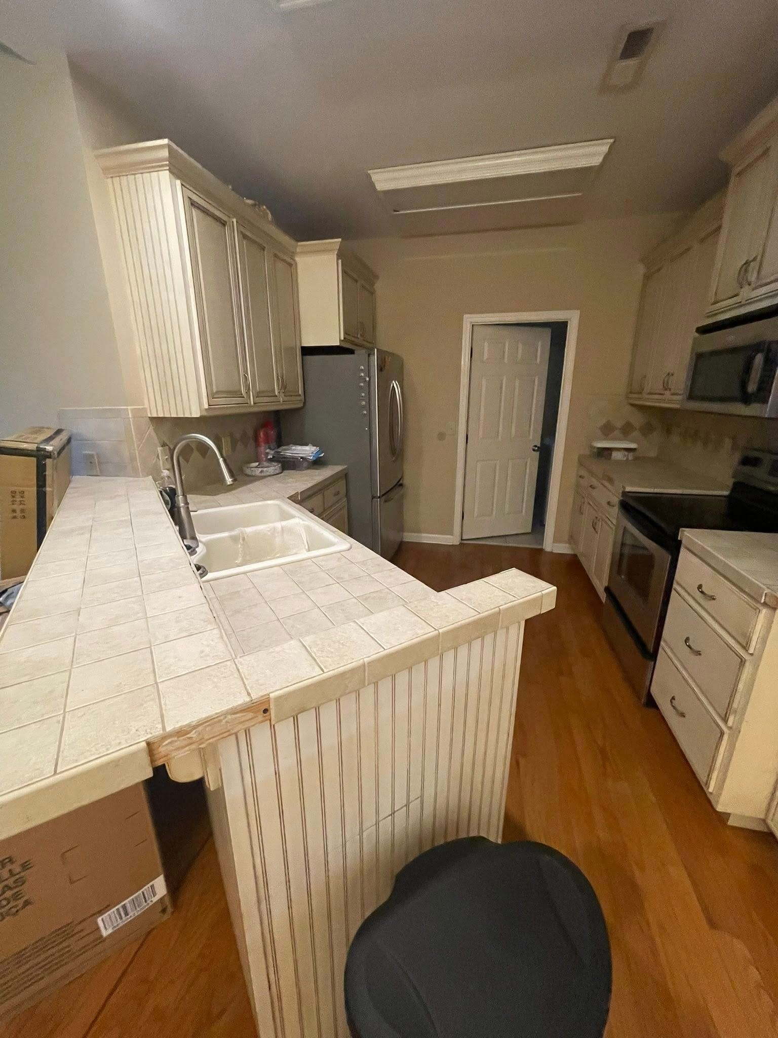Kitchen with cream cabinets, tile countertops, stainless steel appliances, and a white door.