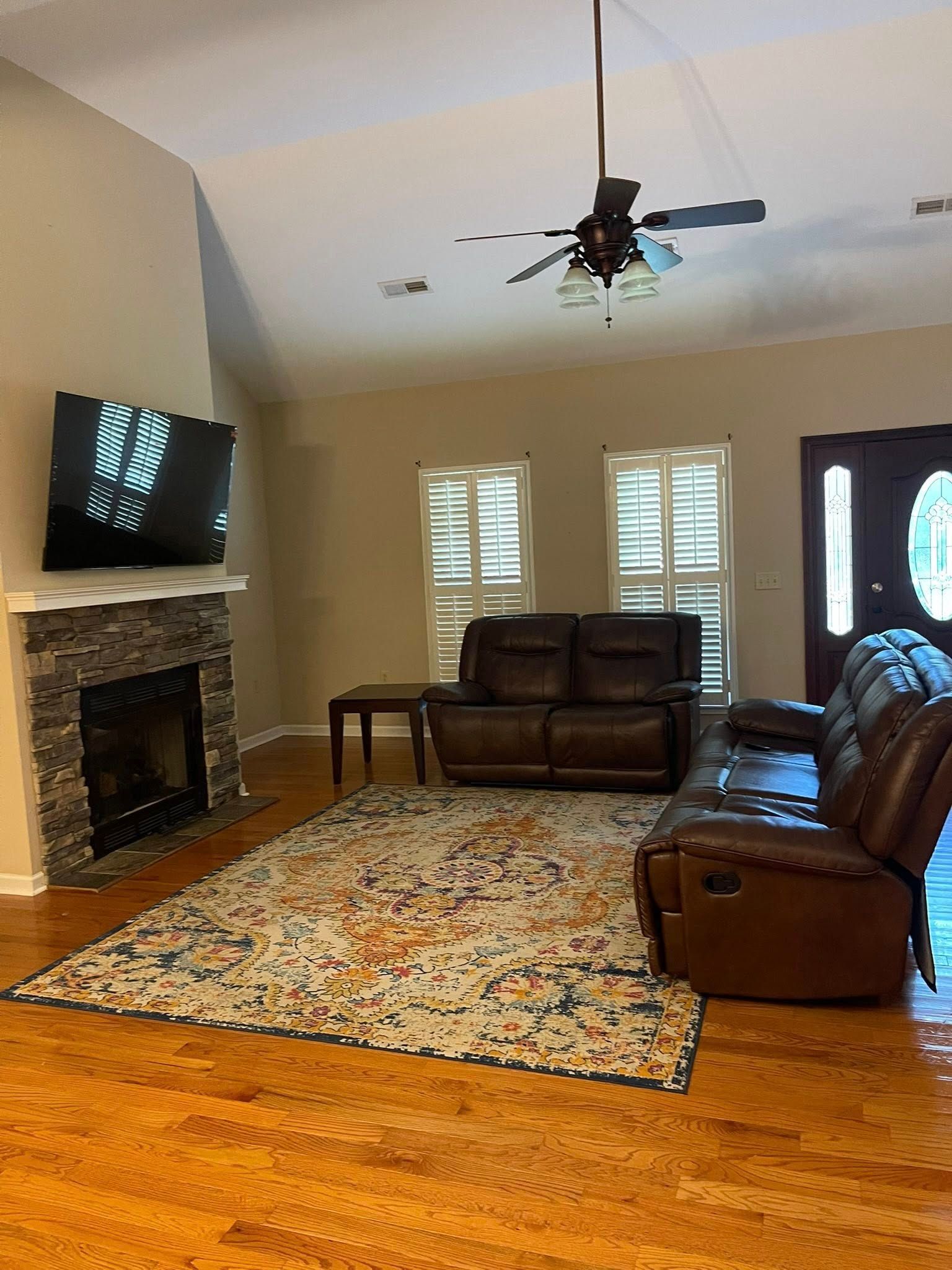 Living room with stone fireplace, brown leather furniture, patterned rug, and wood floors.