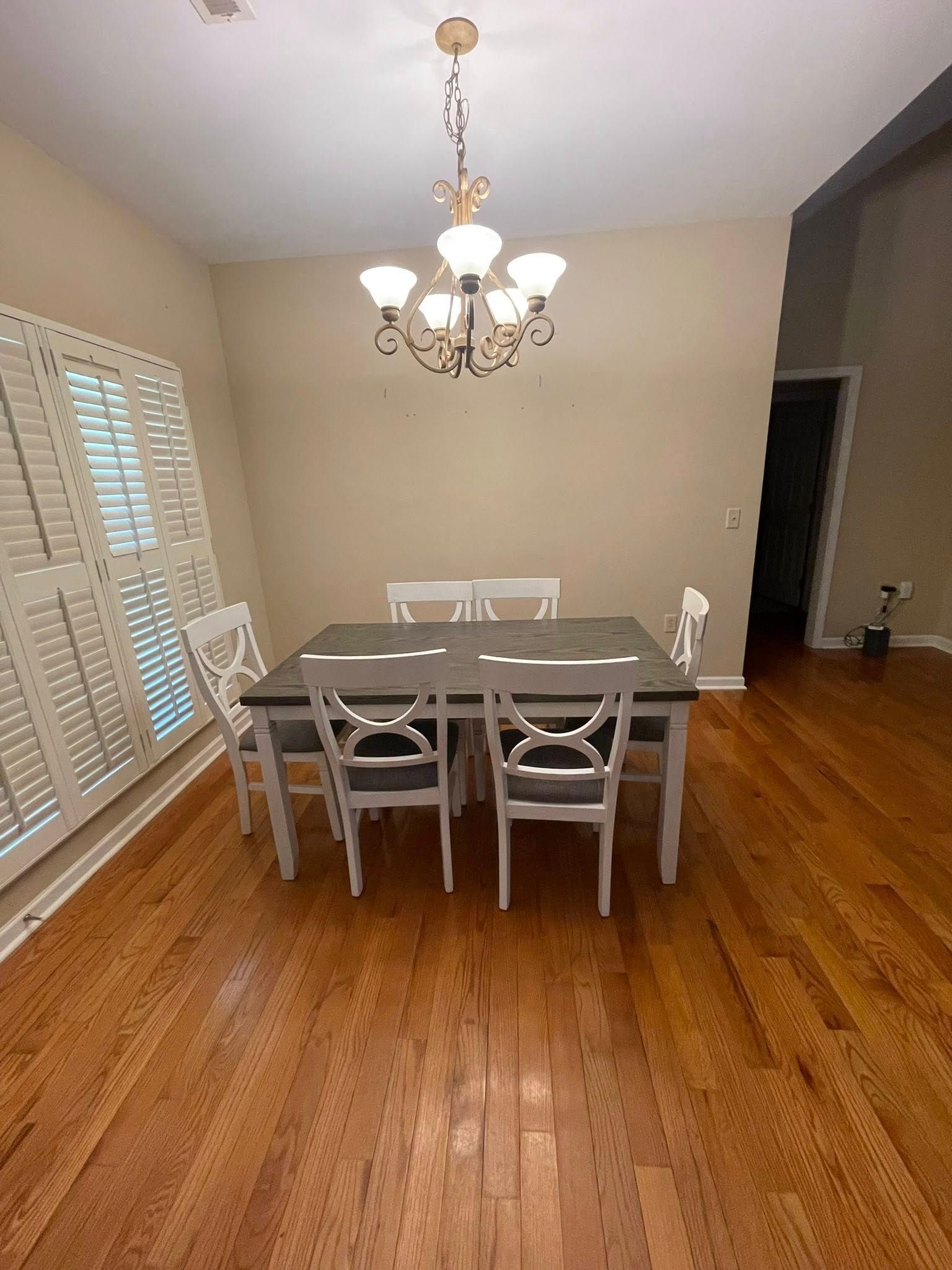 Dining room with a wood table, white chairs, and a chandelier; hardwood floor.