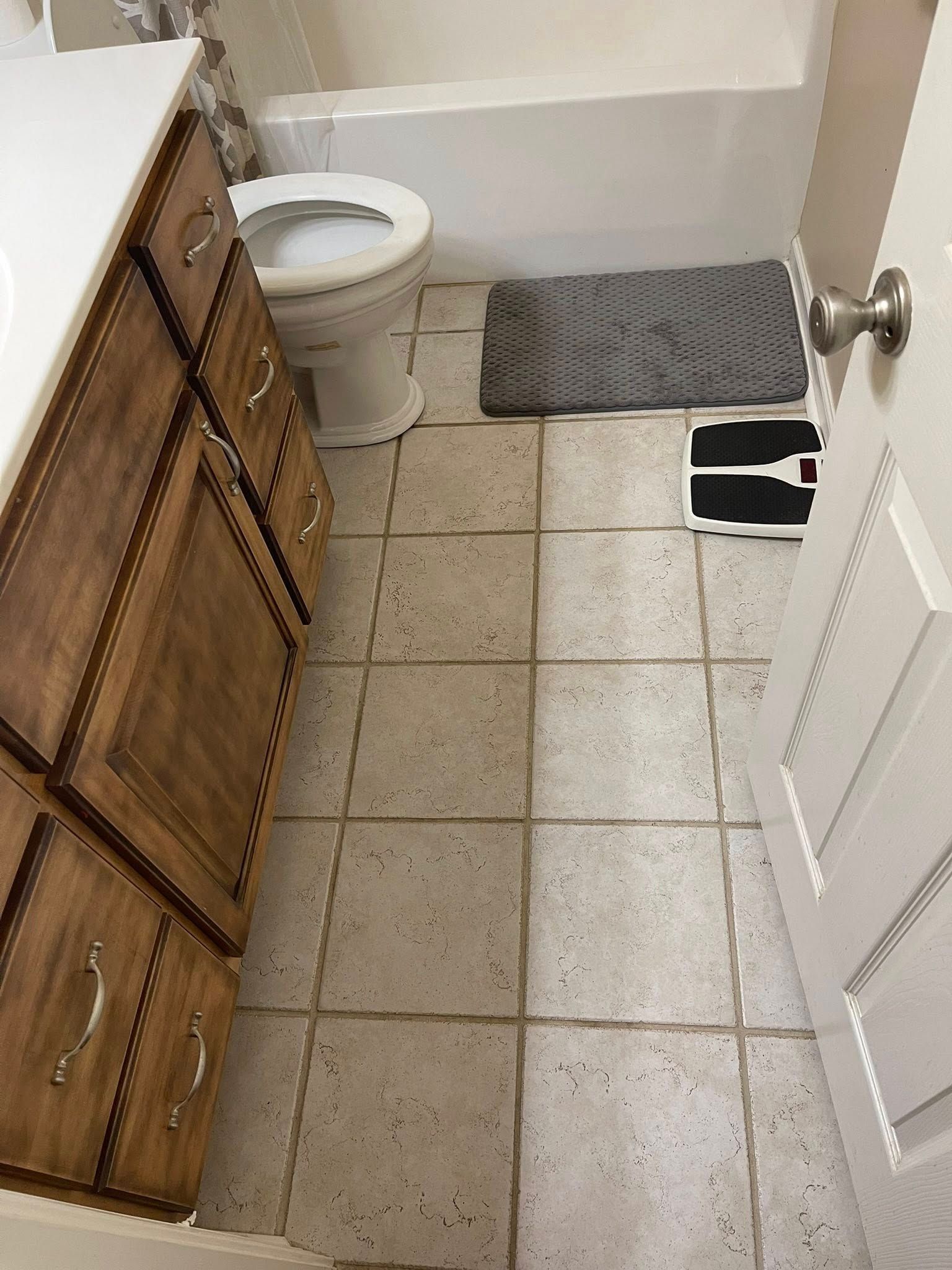 Bathroom with brown cabinets, white toilet, and scale on speckled floor.