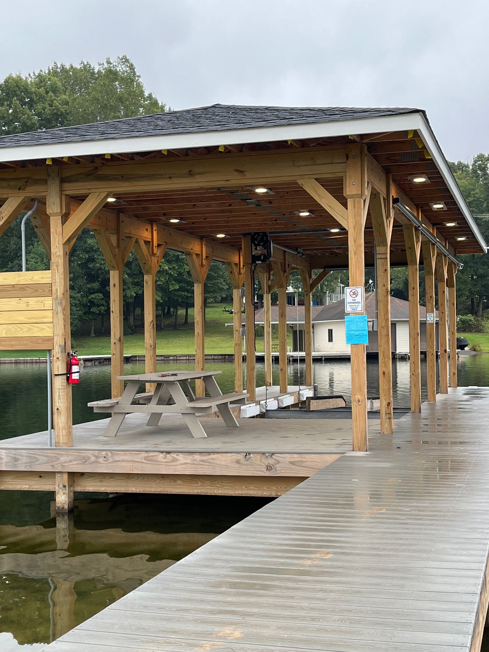 Covered dock with picnic tables, lights, and a fire extinguisher on a lake.