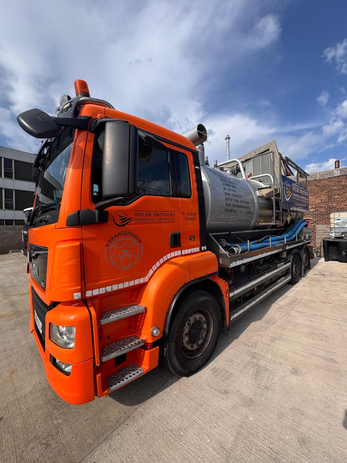 Bright orange industrial truck parked on concrete, under a blue sky.