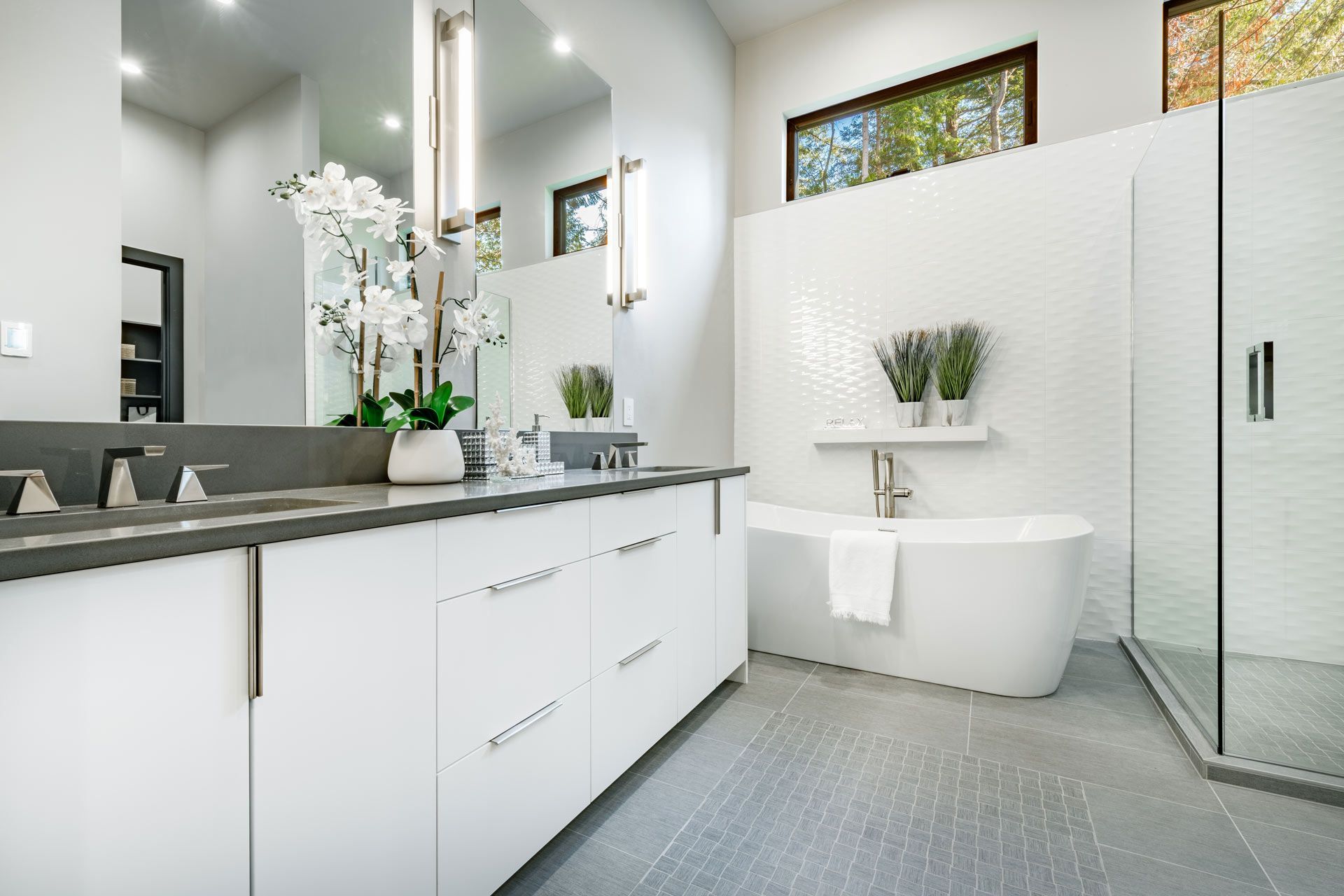 Modern white bathroom with double vanity, freestanding tub, and shower.