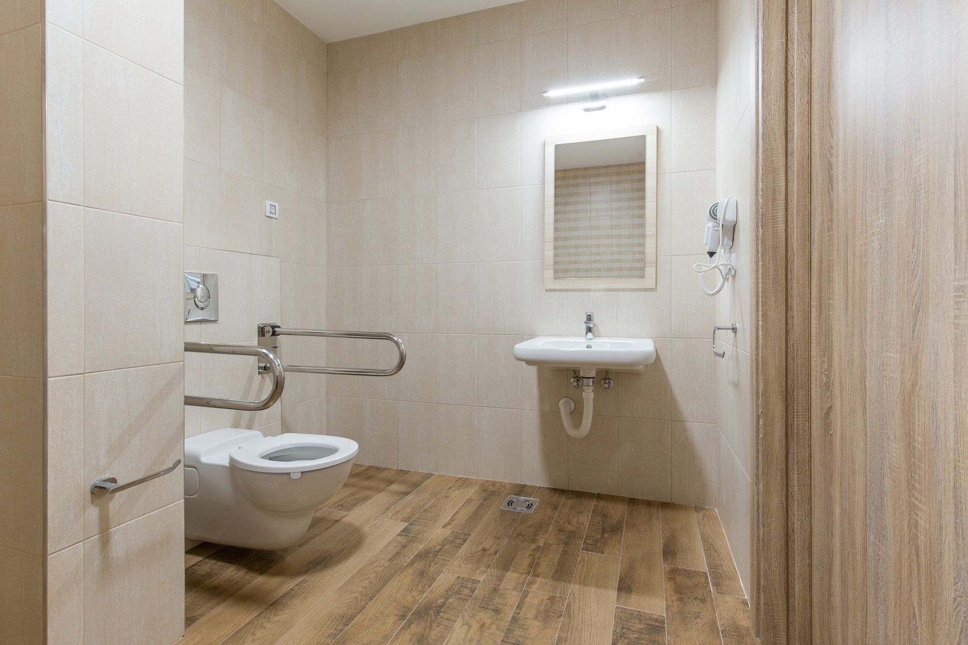 Accessible bathroom with toilet, sink, grab bars, and light wood-look flooring.