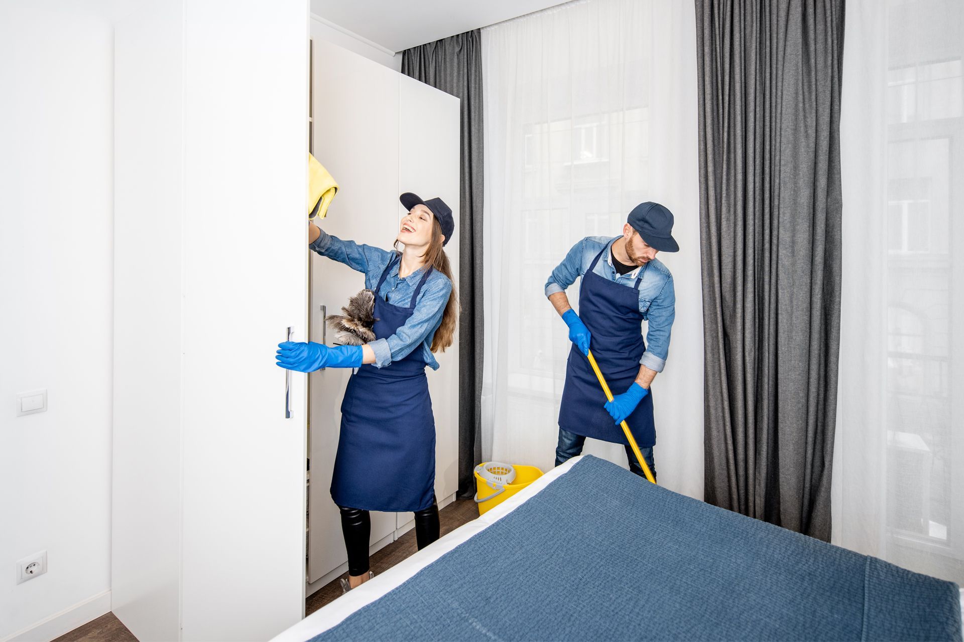 Two people cleaning a room: one wiping a white cabinet, the other mopping the floor.