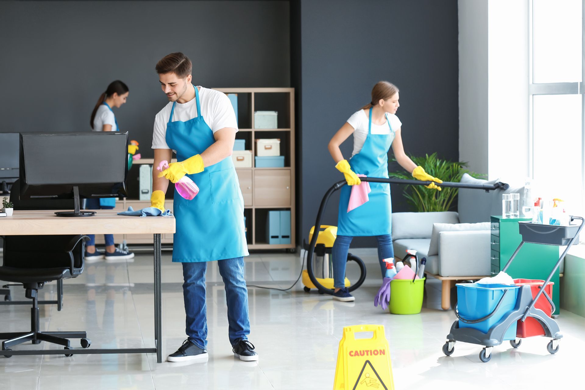 Office cleaners in blue aprons and yellow gloves clean a modern office.