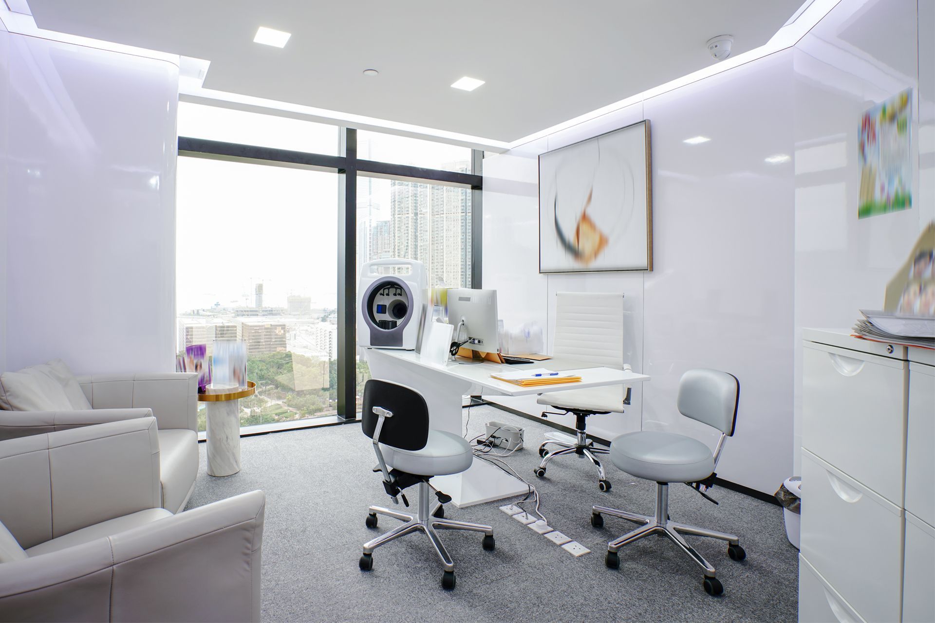 A bright, modern medical room with a desk, chairs, window view, and seating area.