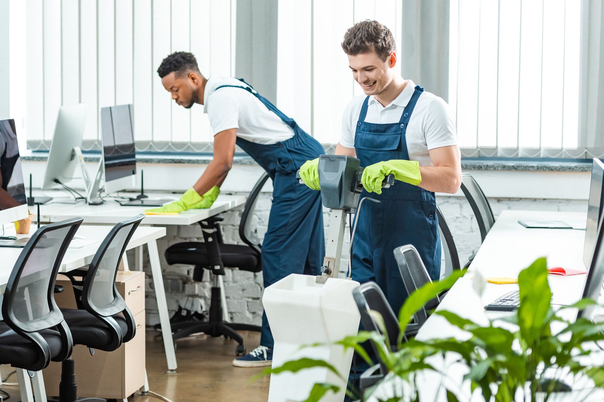 Two people cleaning an office: One wiping a desk, the other using a vacuum.