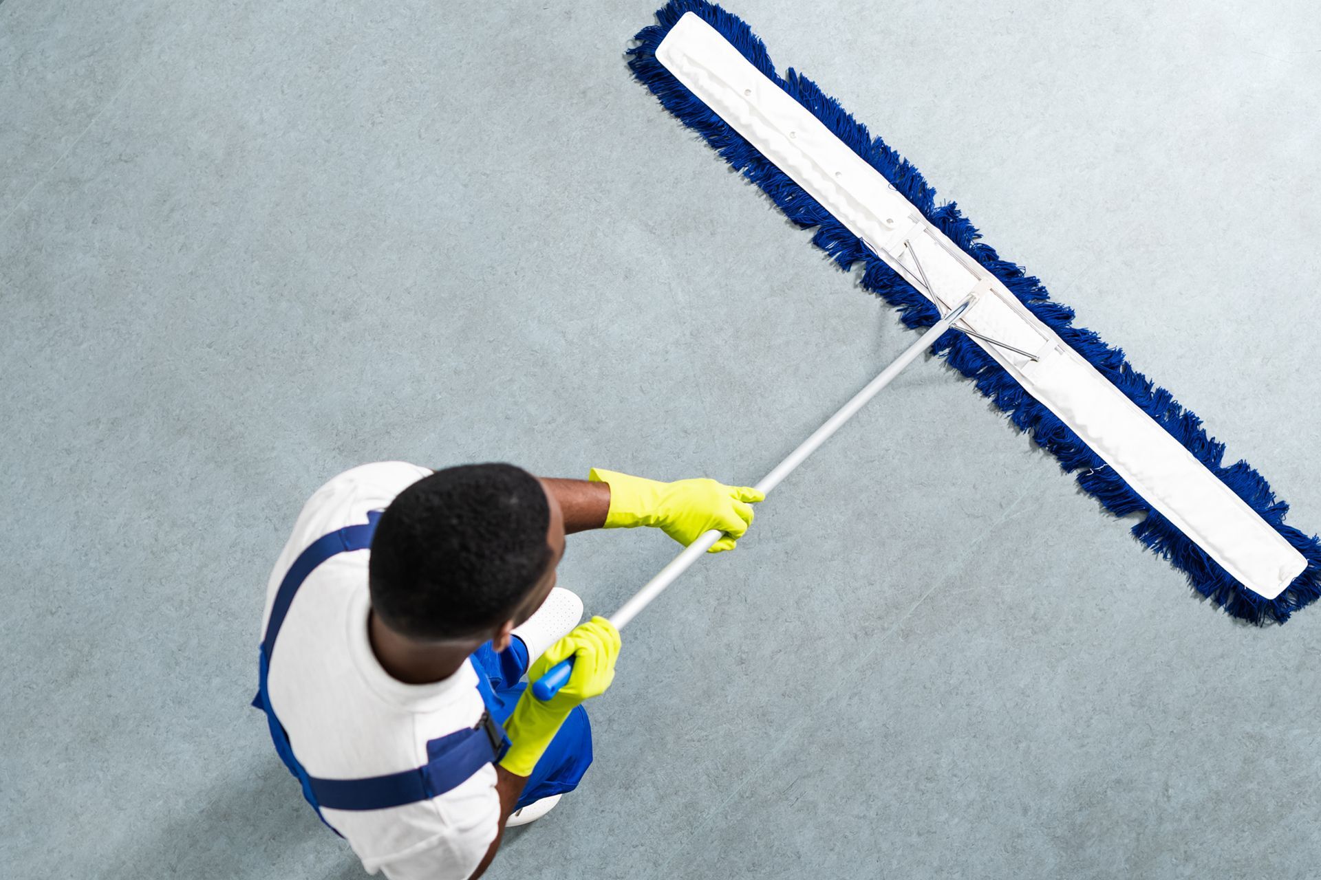 Person in blue and white cleaning a floor with a large, blue-fringed dust mop.