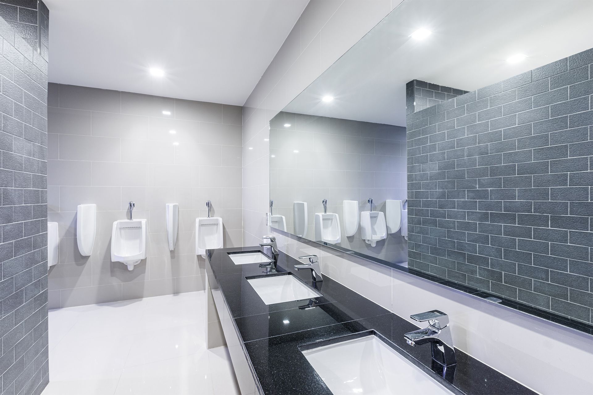 Commercial restroom with urinals, sinks, and large mirror. Gray and white color scheme.