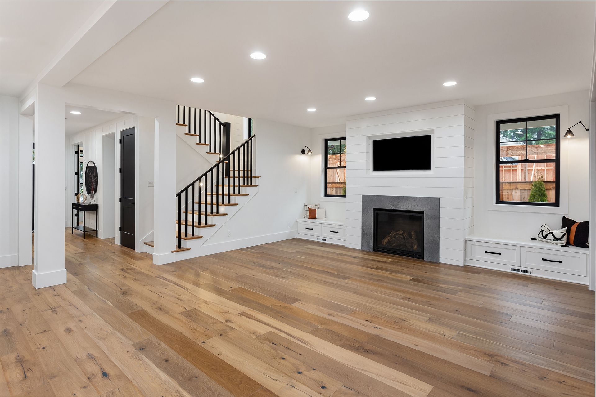 Empty living room with hardwood floors, white walls, fireplace, and staircase.