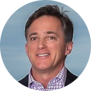 Smiling man in a collared shirt against a light blue background.