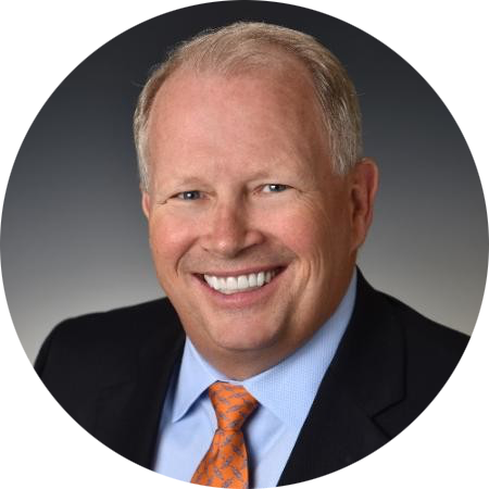 Smiling man in a dark suit and orange tie against a gray background