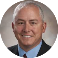 Portrait of a man in a gray suit and striped tie with a U.S. flag backdrop