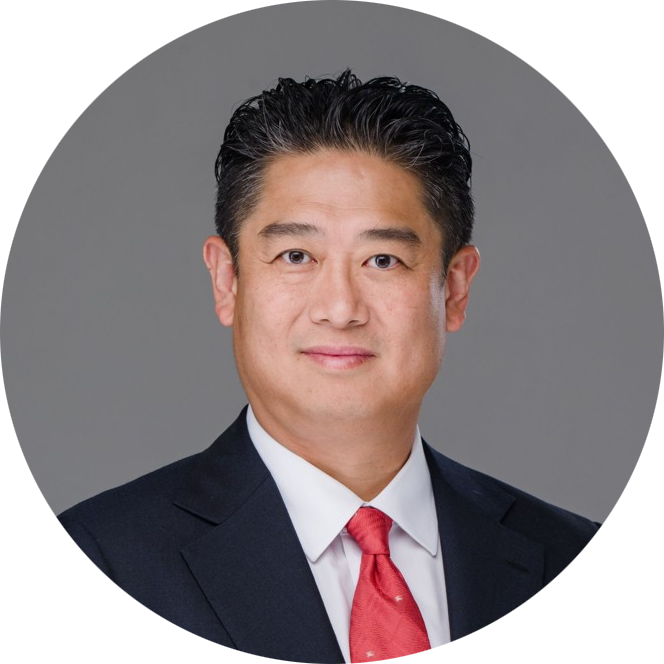 Studio headshot of a man in a dark suit, white shirt, and red tie against a gray background
