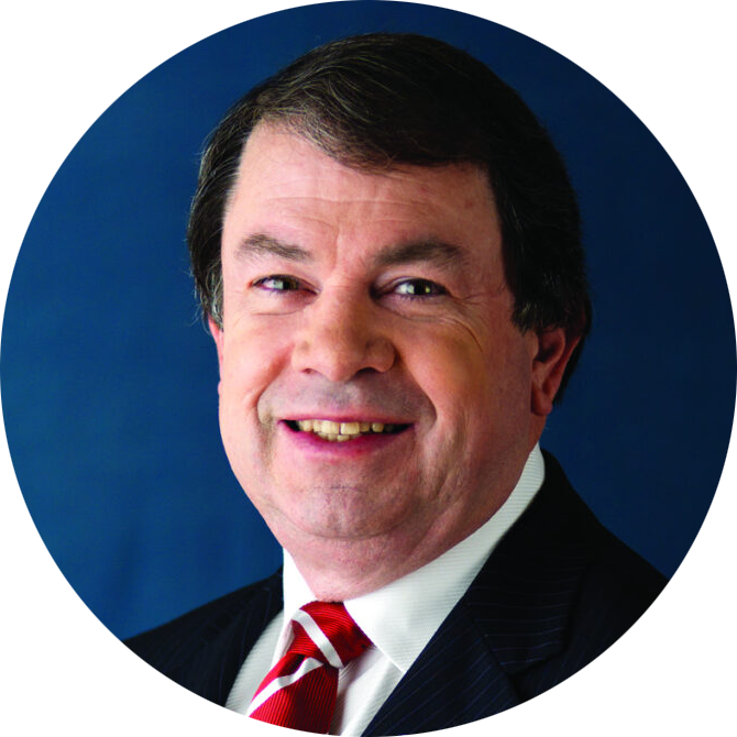 Portrait of a smiling man in a dark suit and red striped tie against a blue background