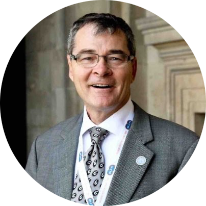 Smiling man in a gray suit and glasses wearing a lanyard at a formal building entrance