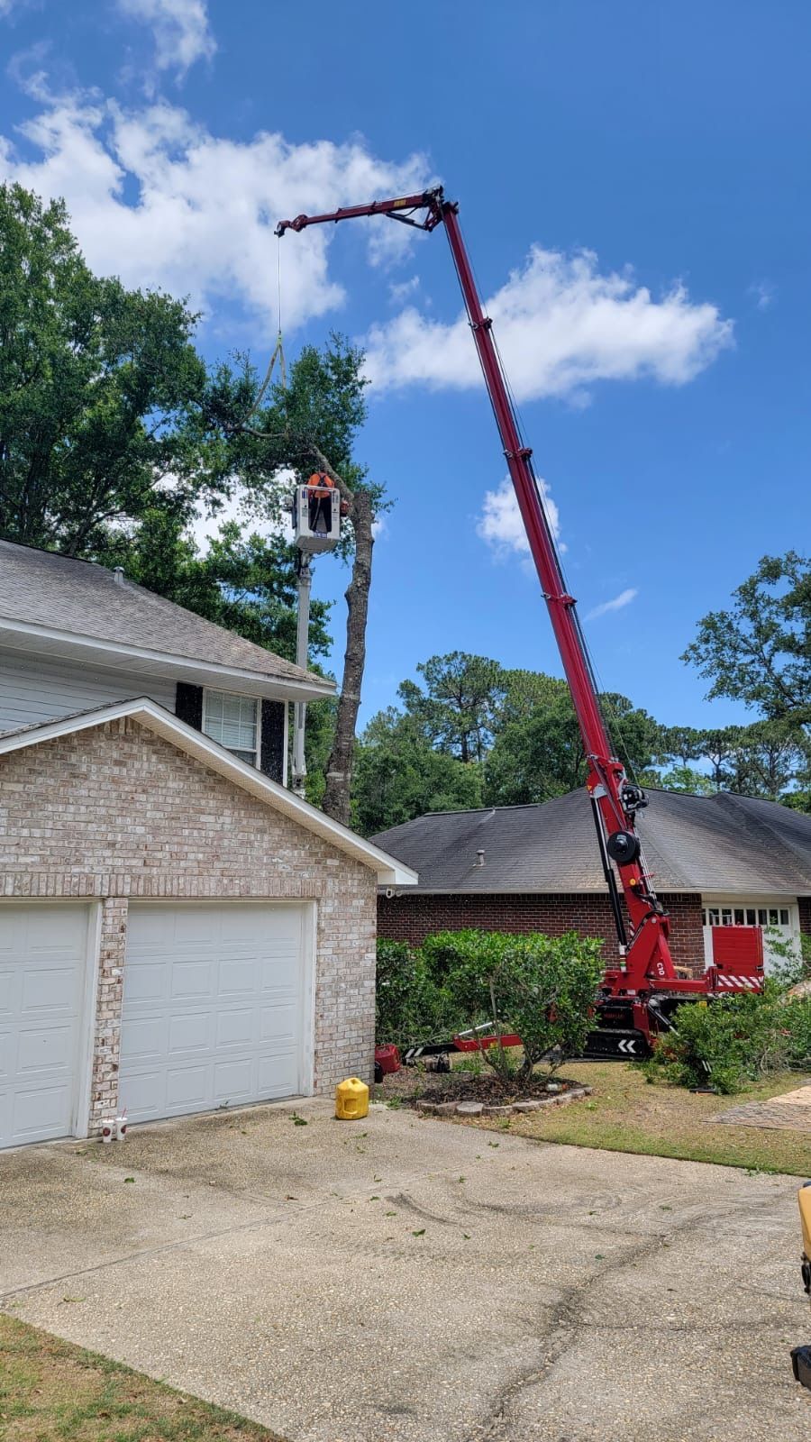 A crane is cutting a tree in front of a house.