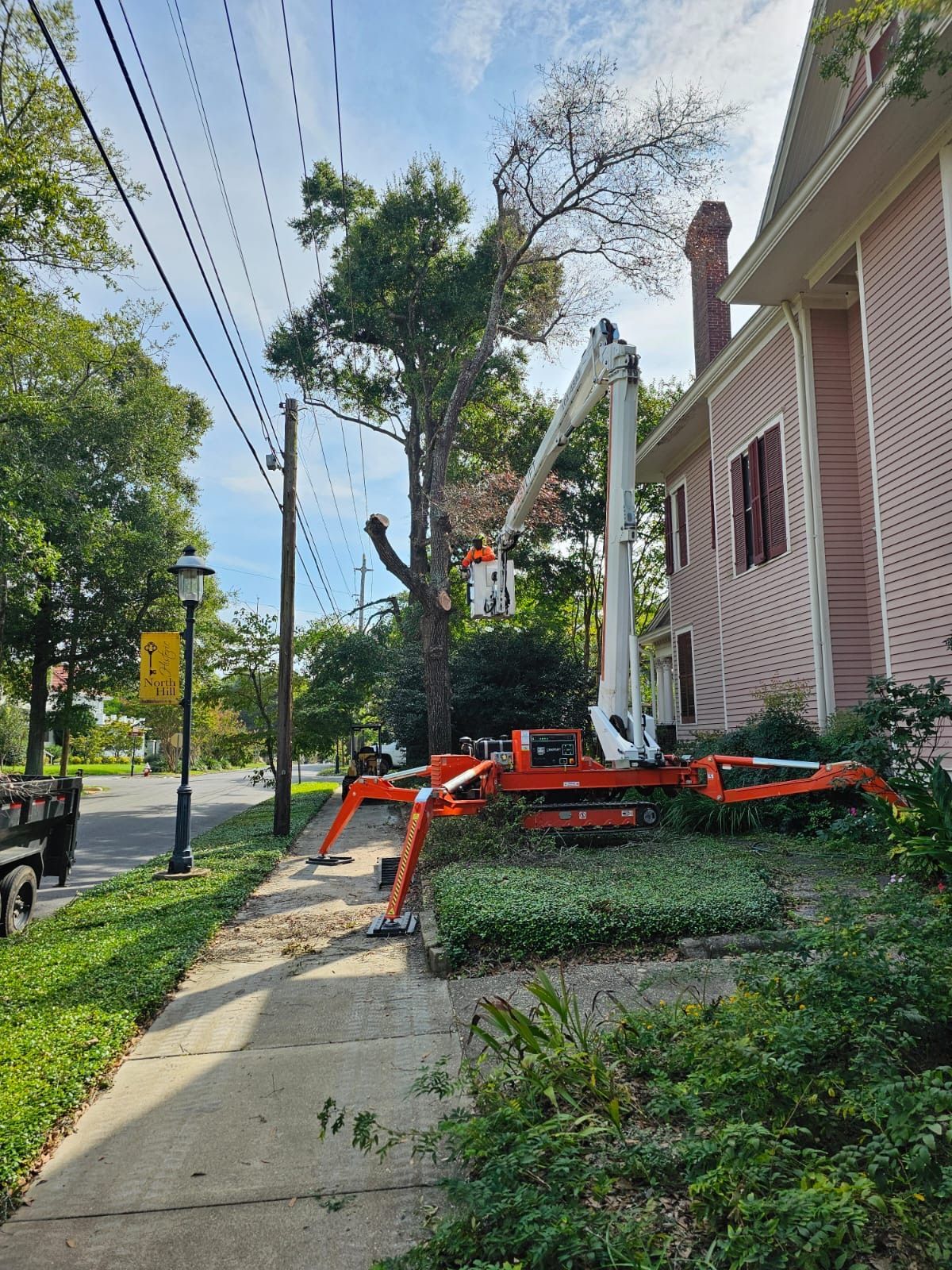 A crane is cutting a tree in front of a house.
