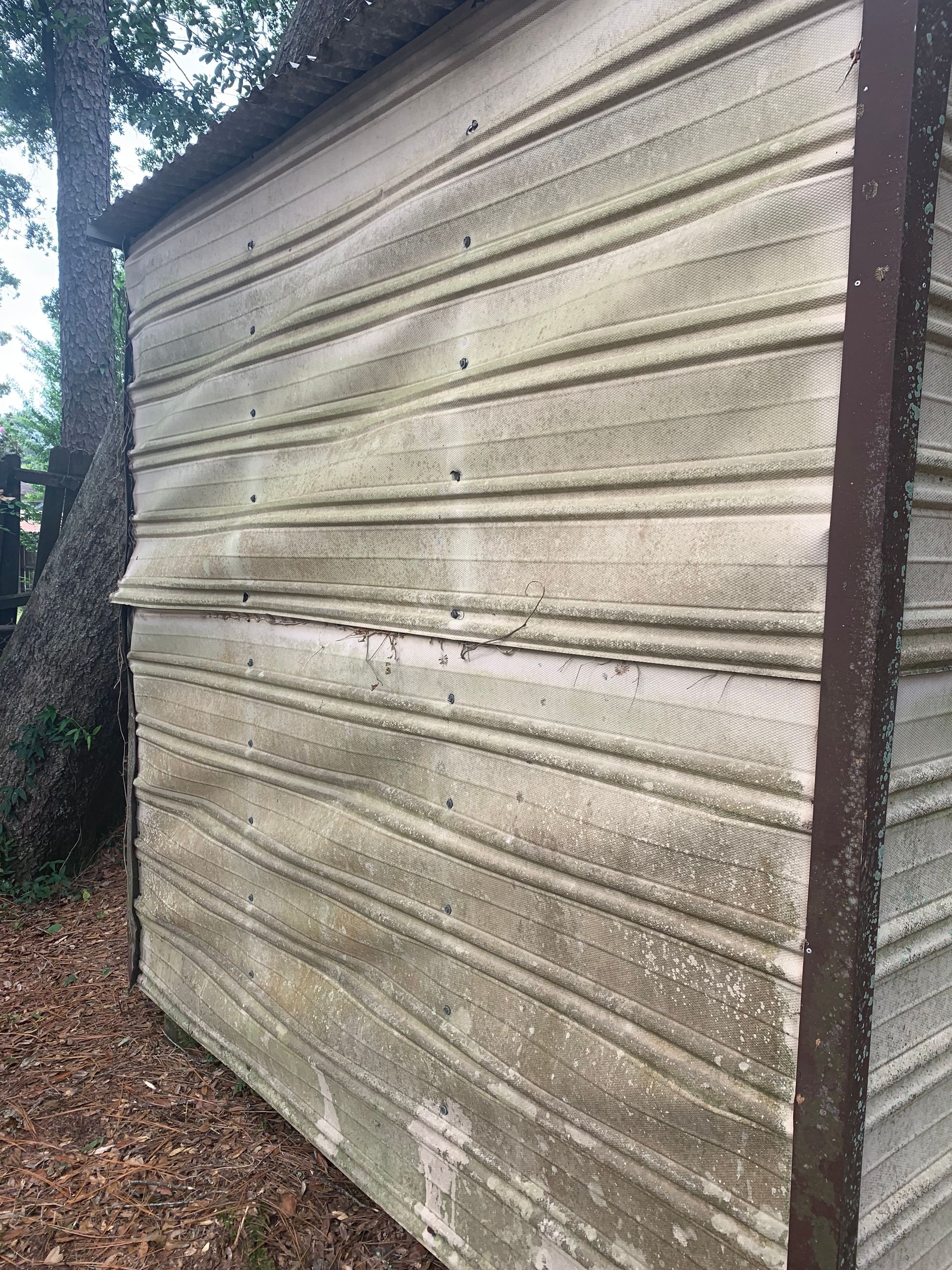 A dirty garage door is sitting in the dirt next to a tree.
