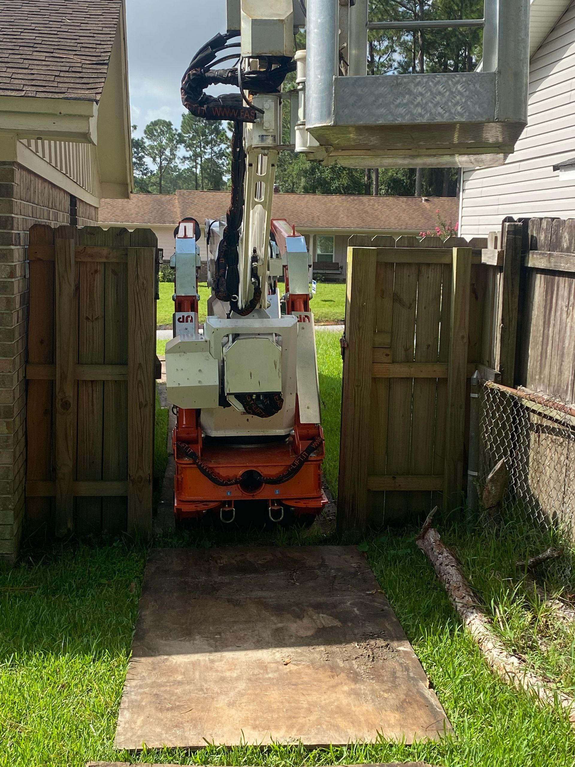 A crane is parked in front of a house next to a wooden fence.