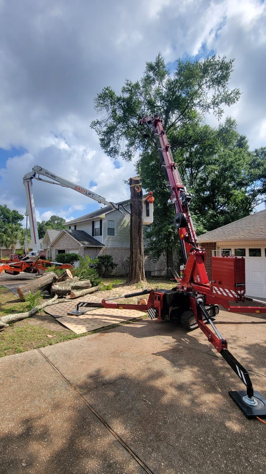 A crane is cutting down a tree in front of a house.